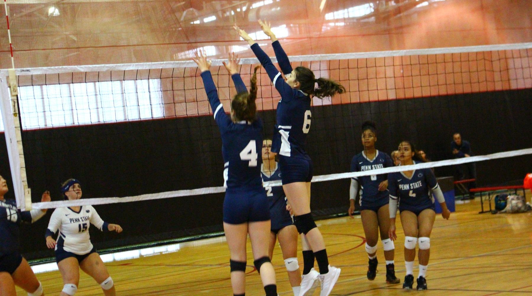 Two TKC volleyball players jump at the net attempting a block.